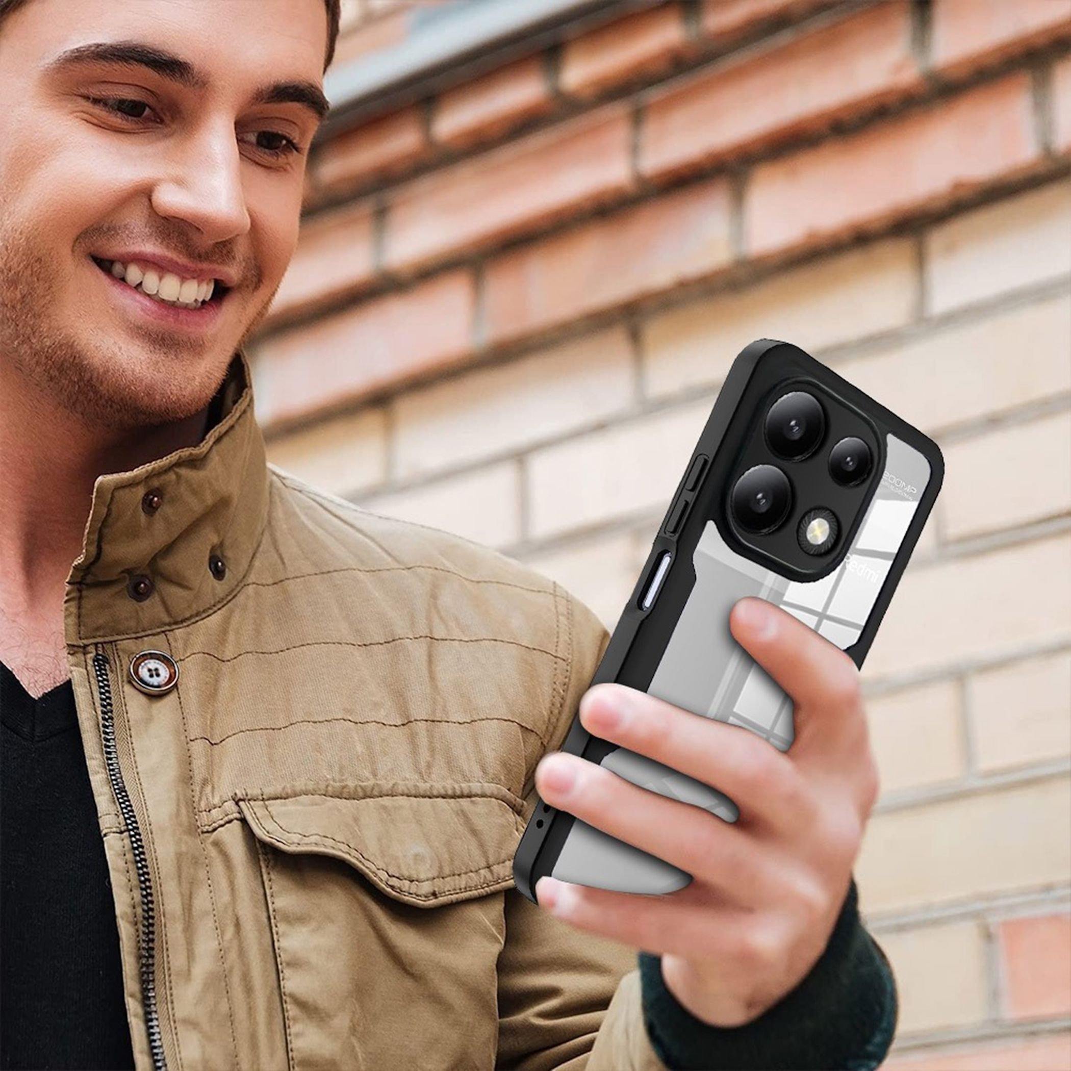 Ein Mann hält ein Smartphone mit schwarzem und durchsichtigem Gehäuse vor einer Ziegelwand.