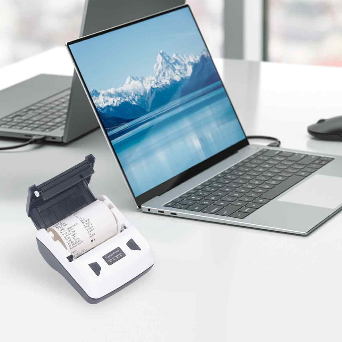 Ein tragbarer Drucker und ein Laptop auf einem Schreibtisch mit Berglandschaft als Hintergrundbild.