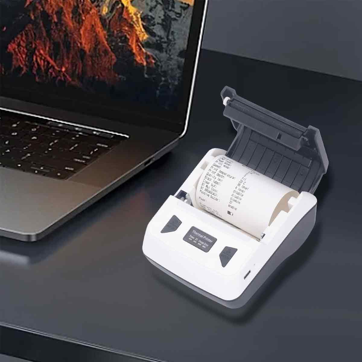 Ein Laptop und ein offener Thermodrucker mit Papierrolle auf einem dunklen Tisch.