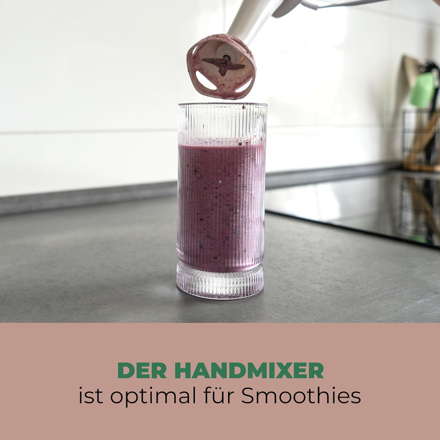 Ein Handmixer wird über einem Glas mit Beeren-Smoothie gehalten.