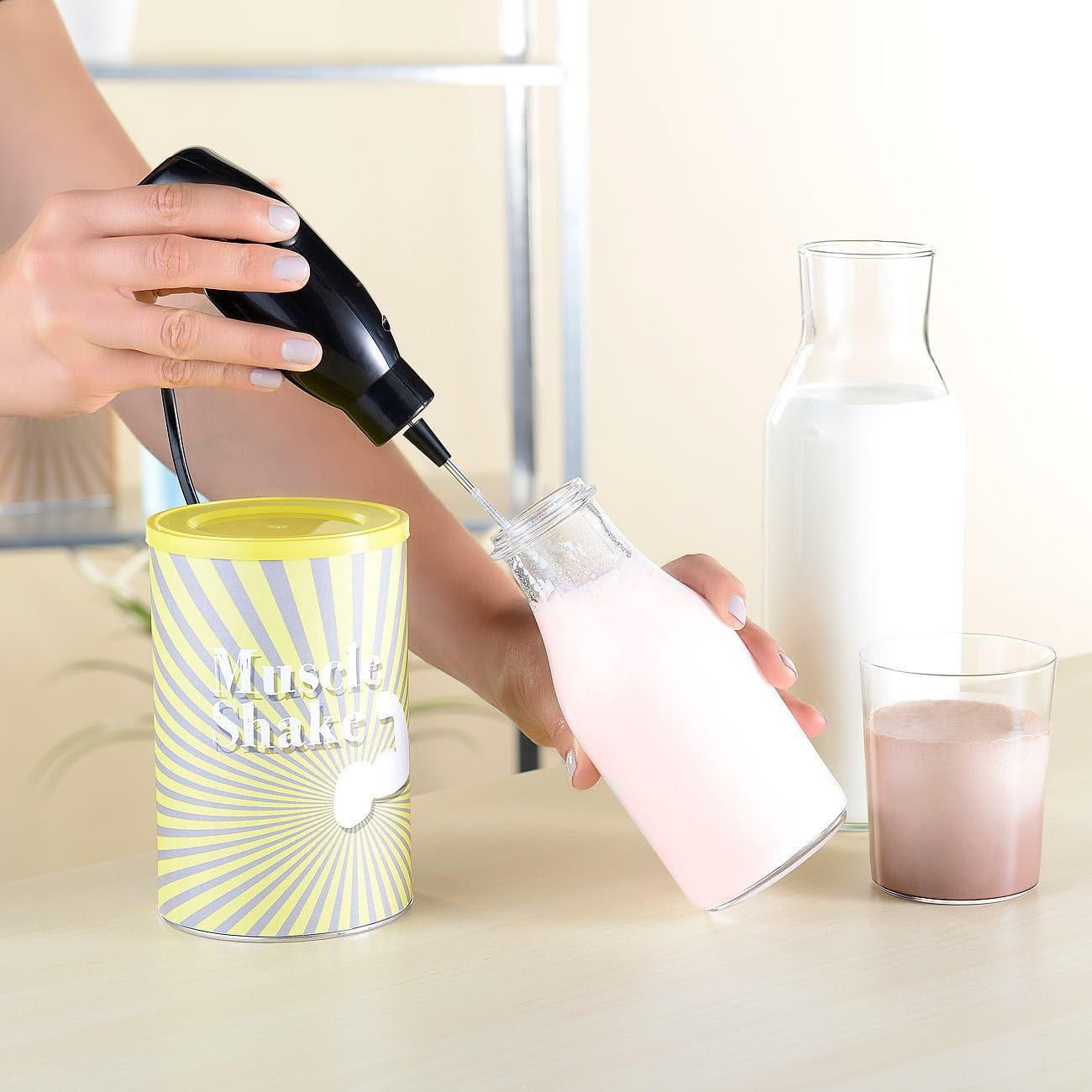 Eine Hand benutzt einen schwarzen Milchaufschäumer in einer Glasflasche mit rosa Flüssigkeit.