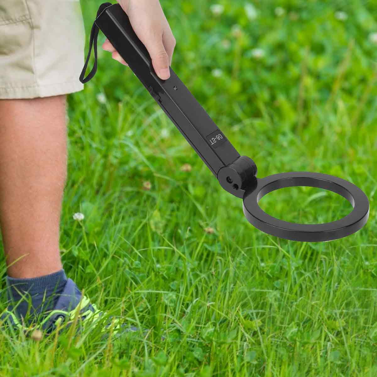Ein Mann hält einen schwarzen Metalldetektor über einem grünen Grasfeld.