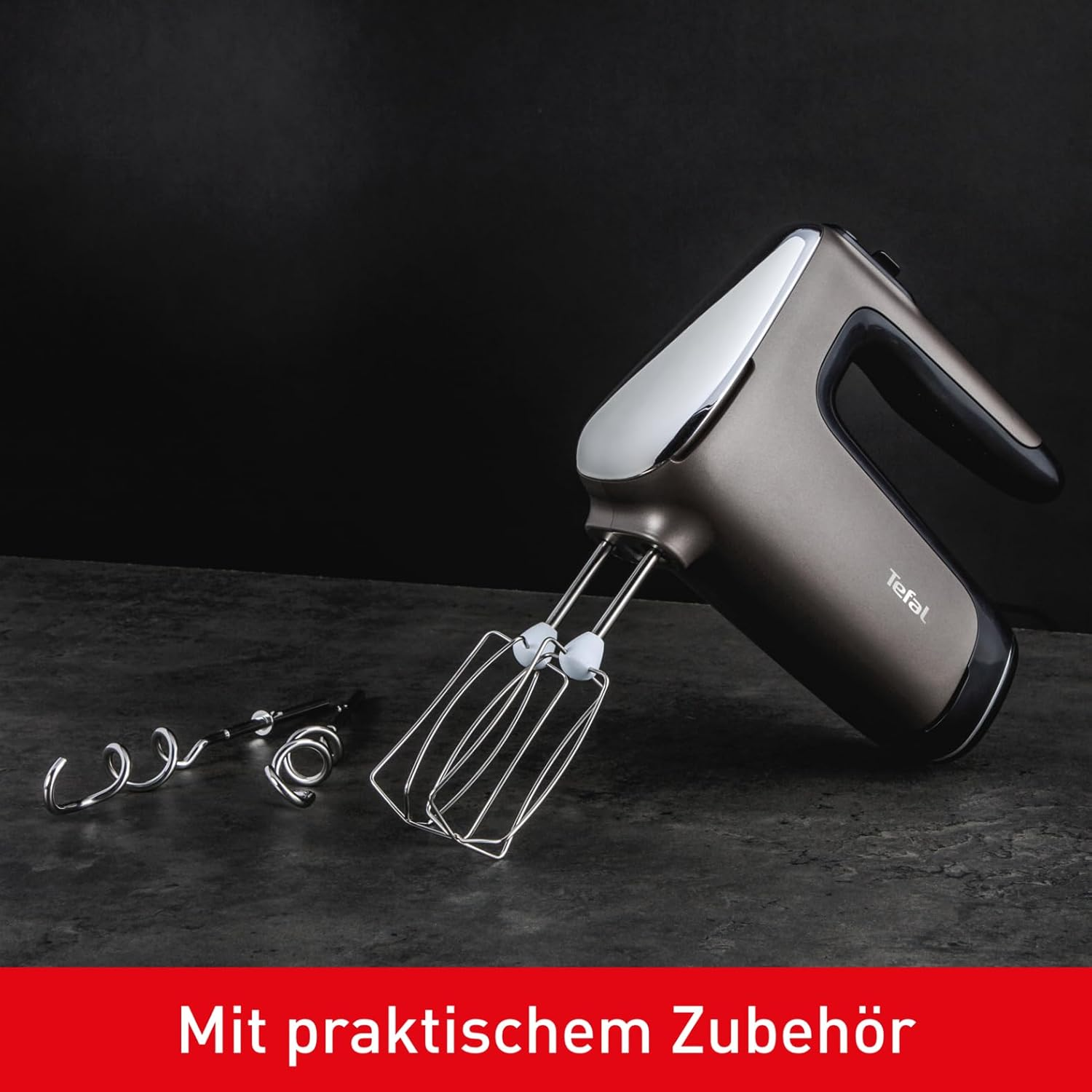 Ein grauer Handmixer mit Schneebesen und Knethaken auf dunklem Untergrund.