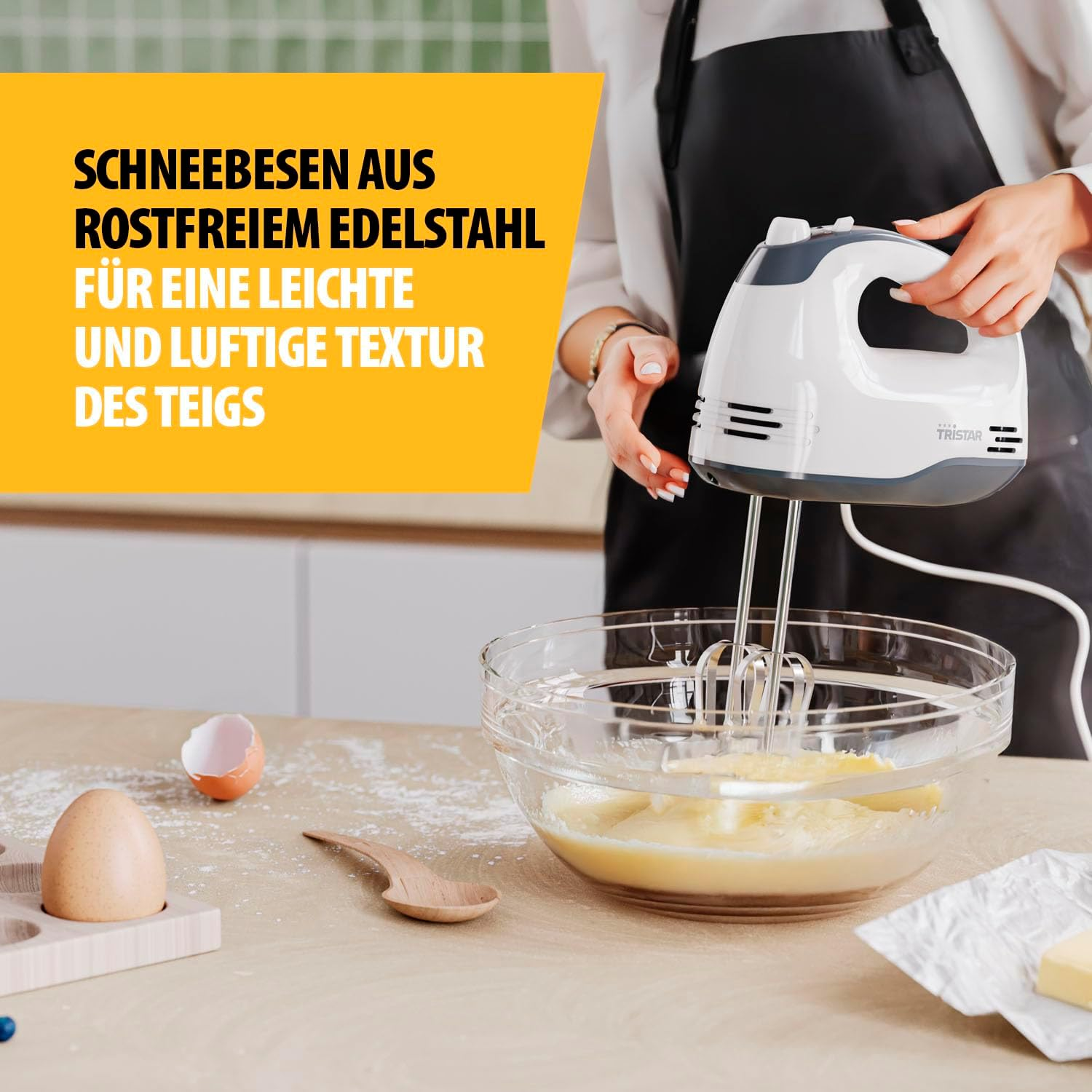 Ein Handmixer rührt Teig in einer Glasschüssel, daneben ein Ei und eine Schale.