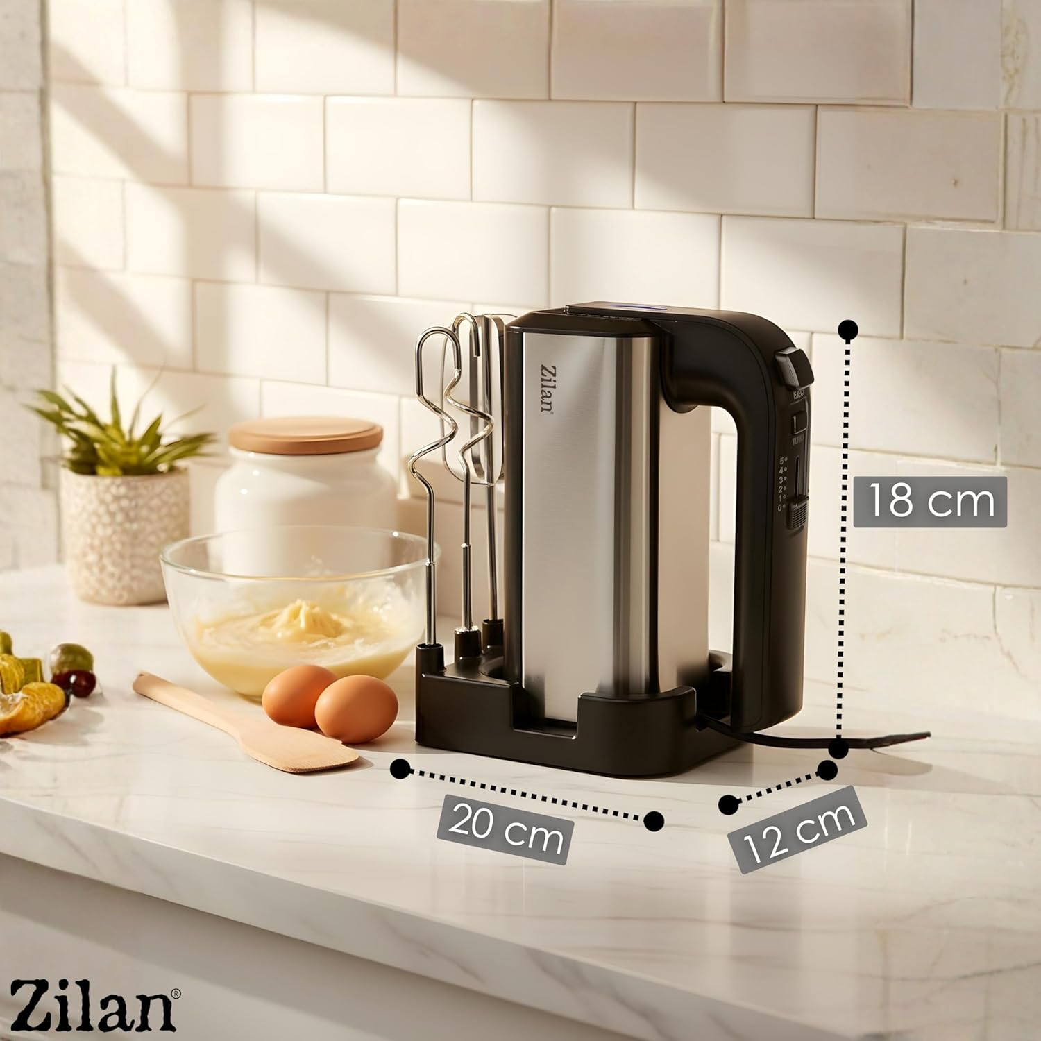 Edelstahl-Handmixer mit schwarzem Griff auf einer Arbeitsplatte neben Eiern und Schüssel.