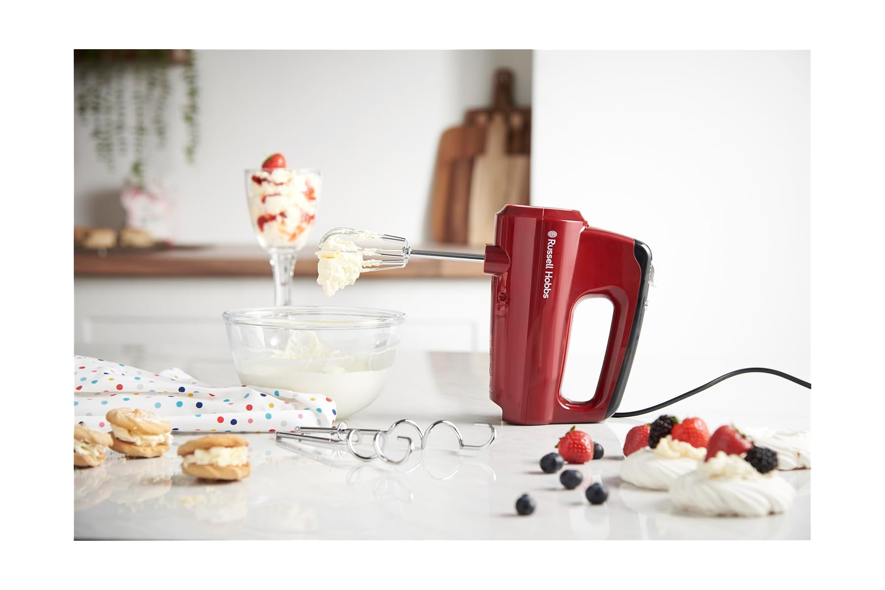 Ein roter Handmixer mit Rührbesen, der Sahne aus einer Schüssel hebt.