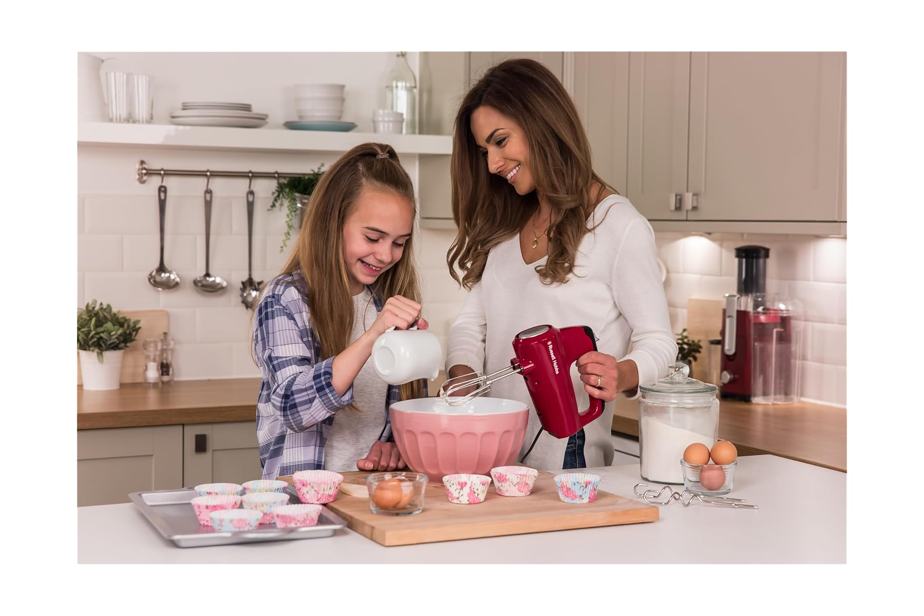 Mutter und Tochter backen zusammen in einer Küche mit einem roten Handmixer.