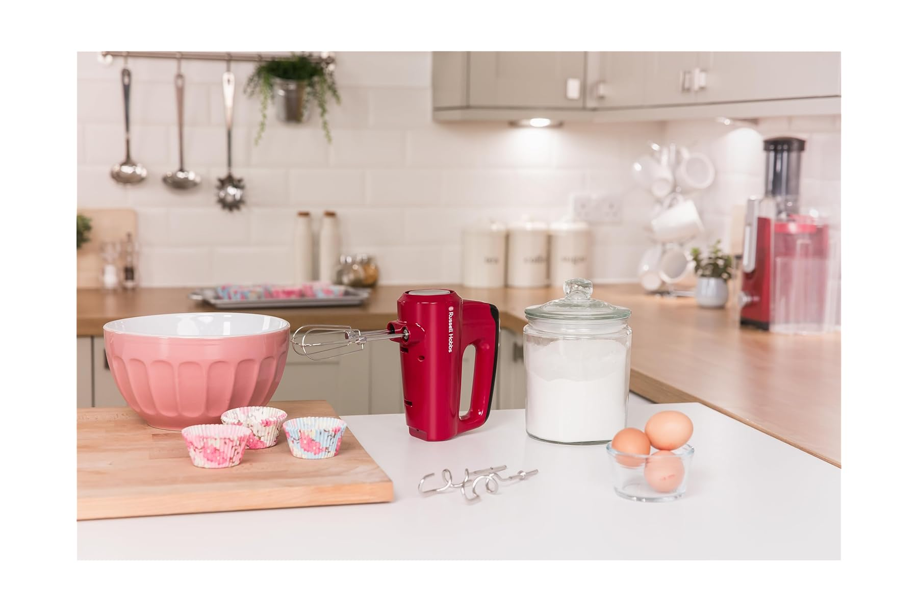 Ein rotes Handrührgerät mit Schüssel, Cupcakes, Eiern und Mehl in einer Küche.