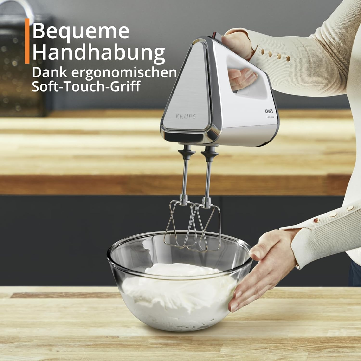 Eine Hand hält einen weißen Krups Handmixer über einer Glasschüssel mit Schlagsahne.