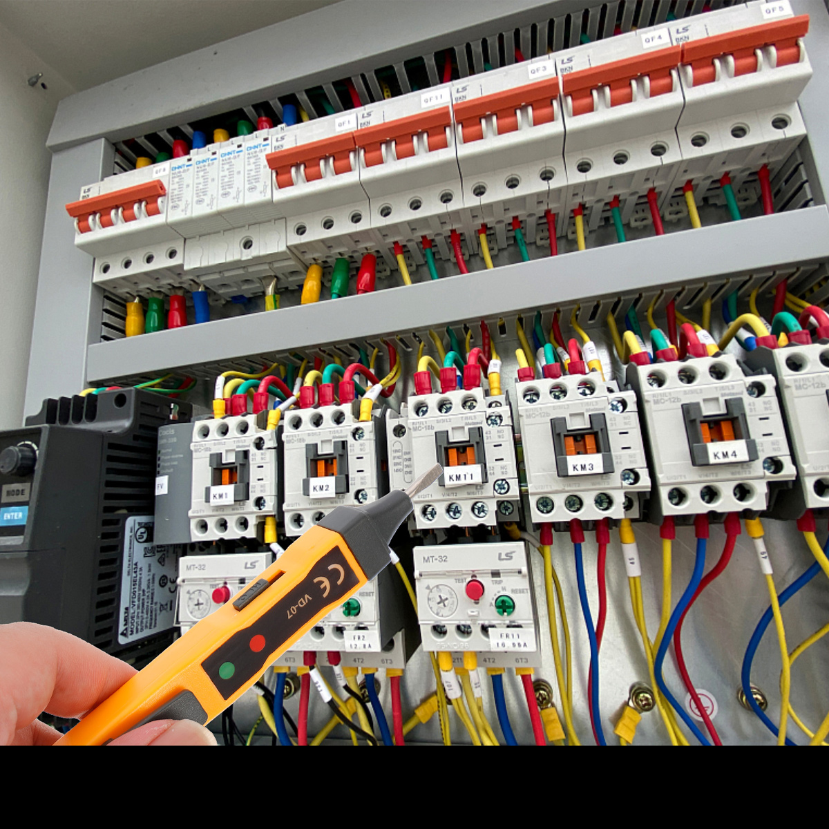 Ein orangefarbener Spannungsprüfer in der Nähe einer elektrischen Schalttafel mit vielen Schaltern und Kabeln.