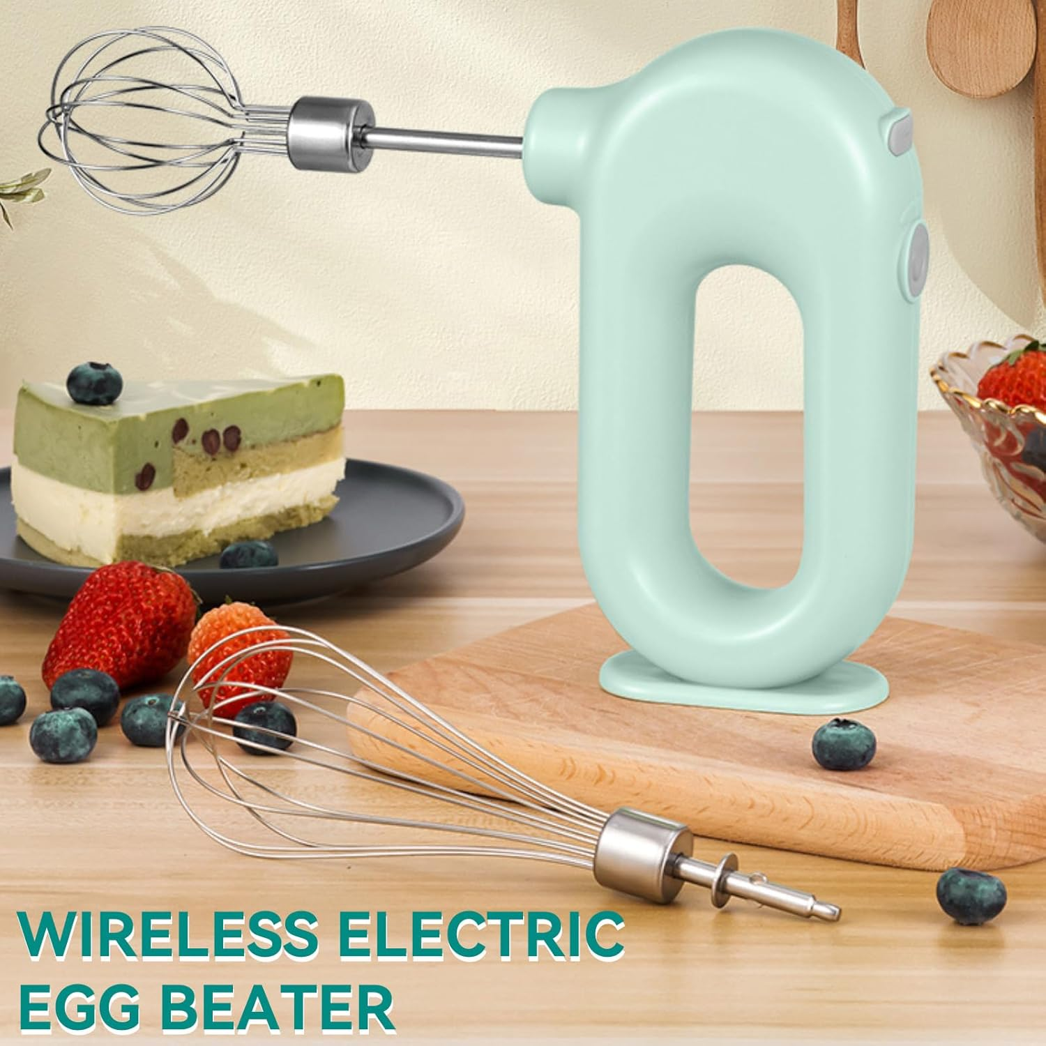 Ein mintgrüner kabelloser Handmixer mit Schneebesen und Kuchen auf einem Tisch.