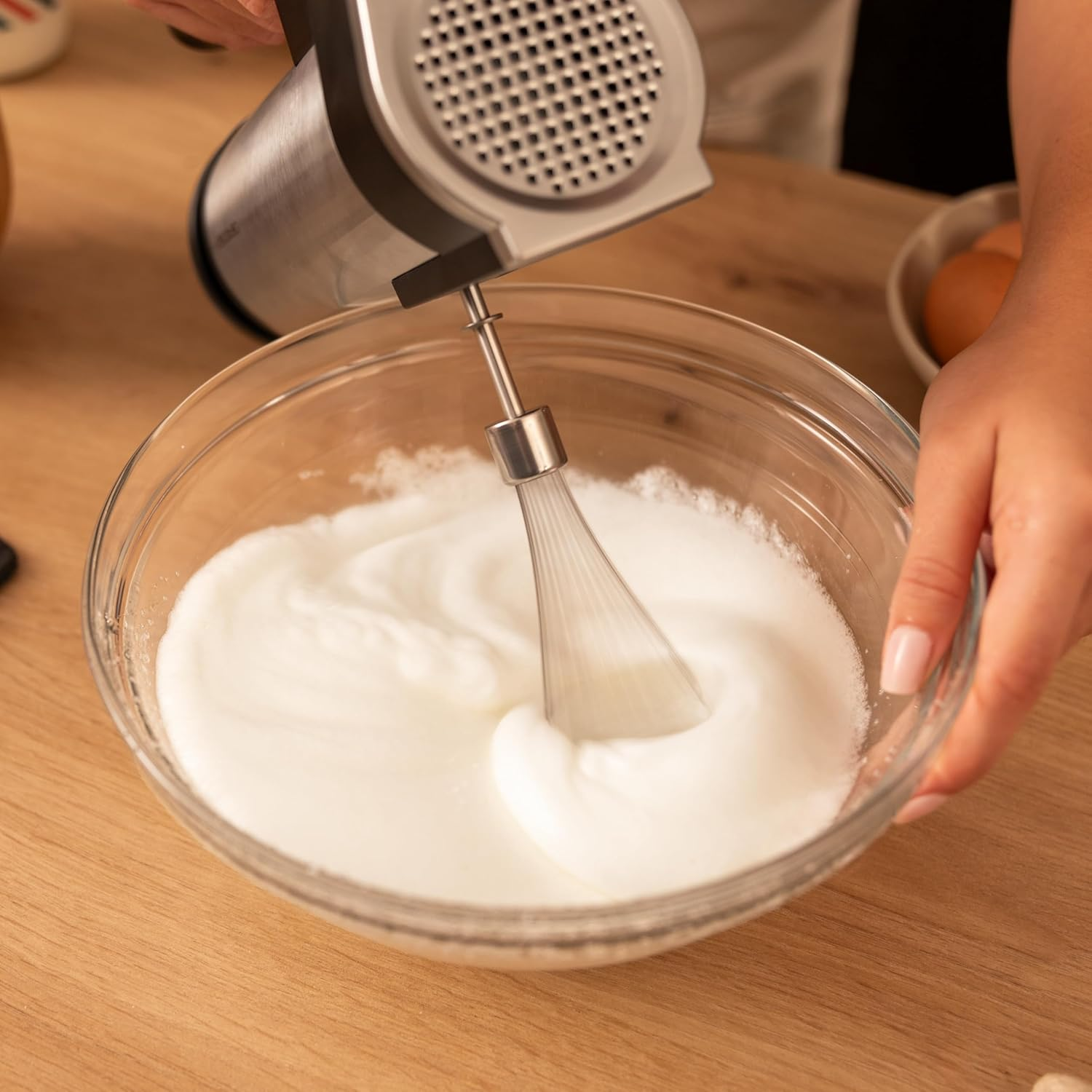 Eine Hand hält einen Handmixer, der Eischnee in einer Glasschüssel schlägt.