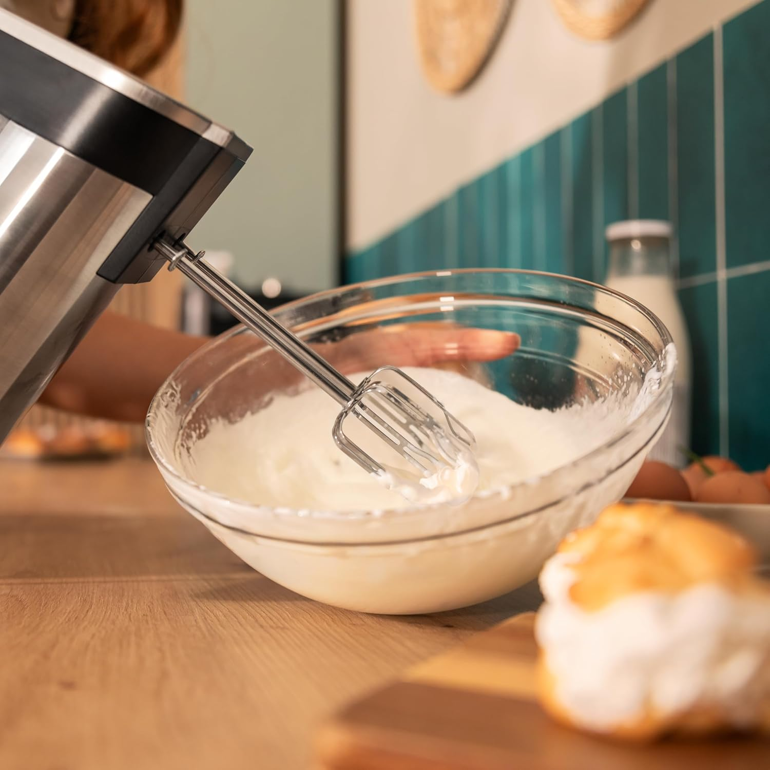 Ein Handmixer schlägt Sahne in einer Glasschüssel auf einem Holztisch.