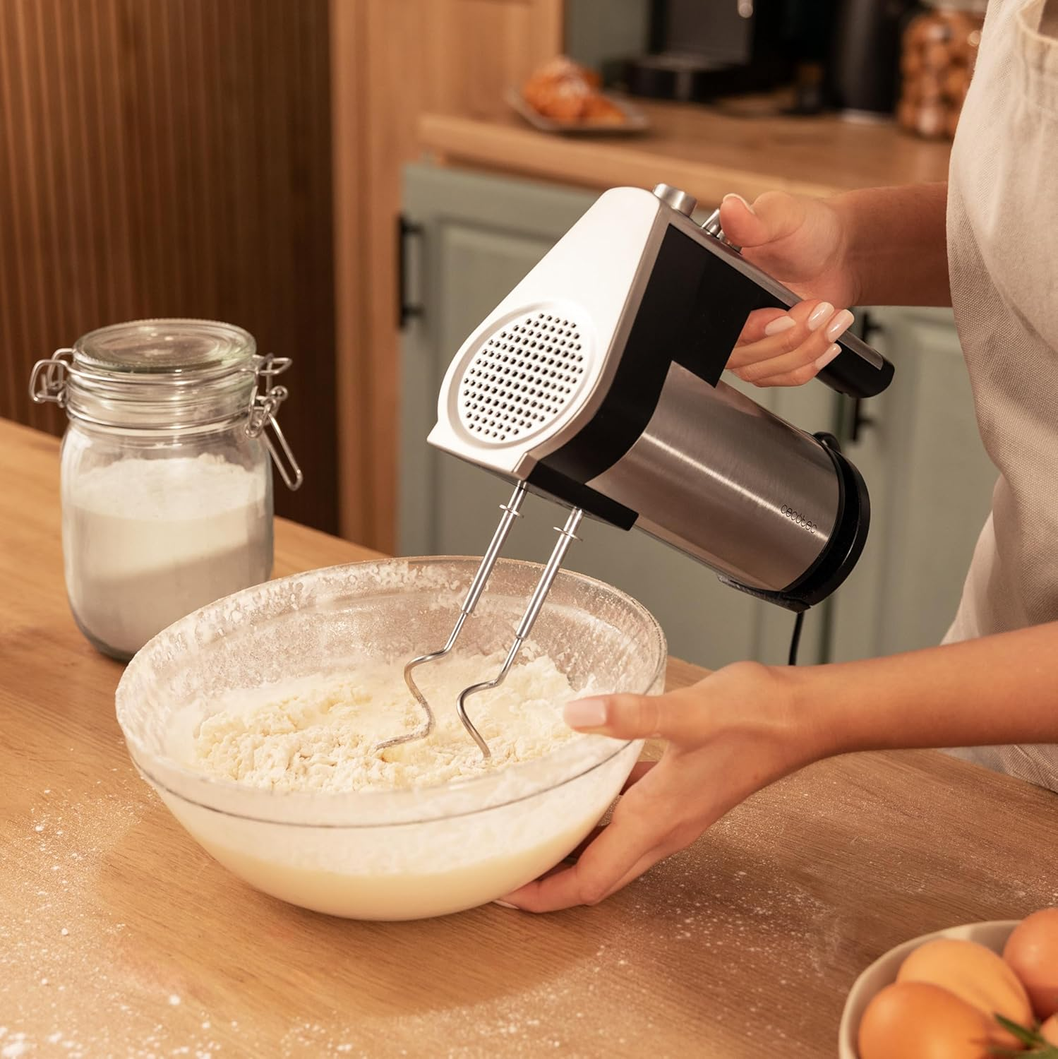 Eine Hand benutzt einen Handmixer, um Teig in einer Schüssel zu mischen. Ein Glas Mehl steht daneben.