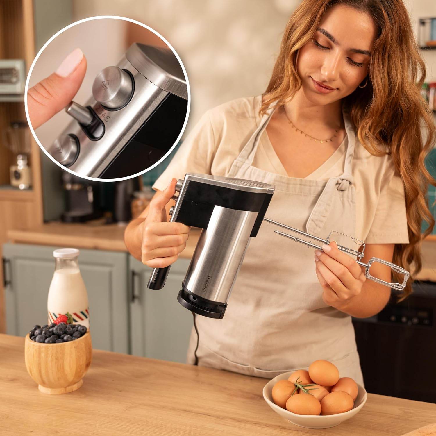 Frau hält einen silbernen Handmixer, daneben Blaubeeren, Milch und Eier.