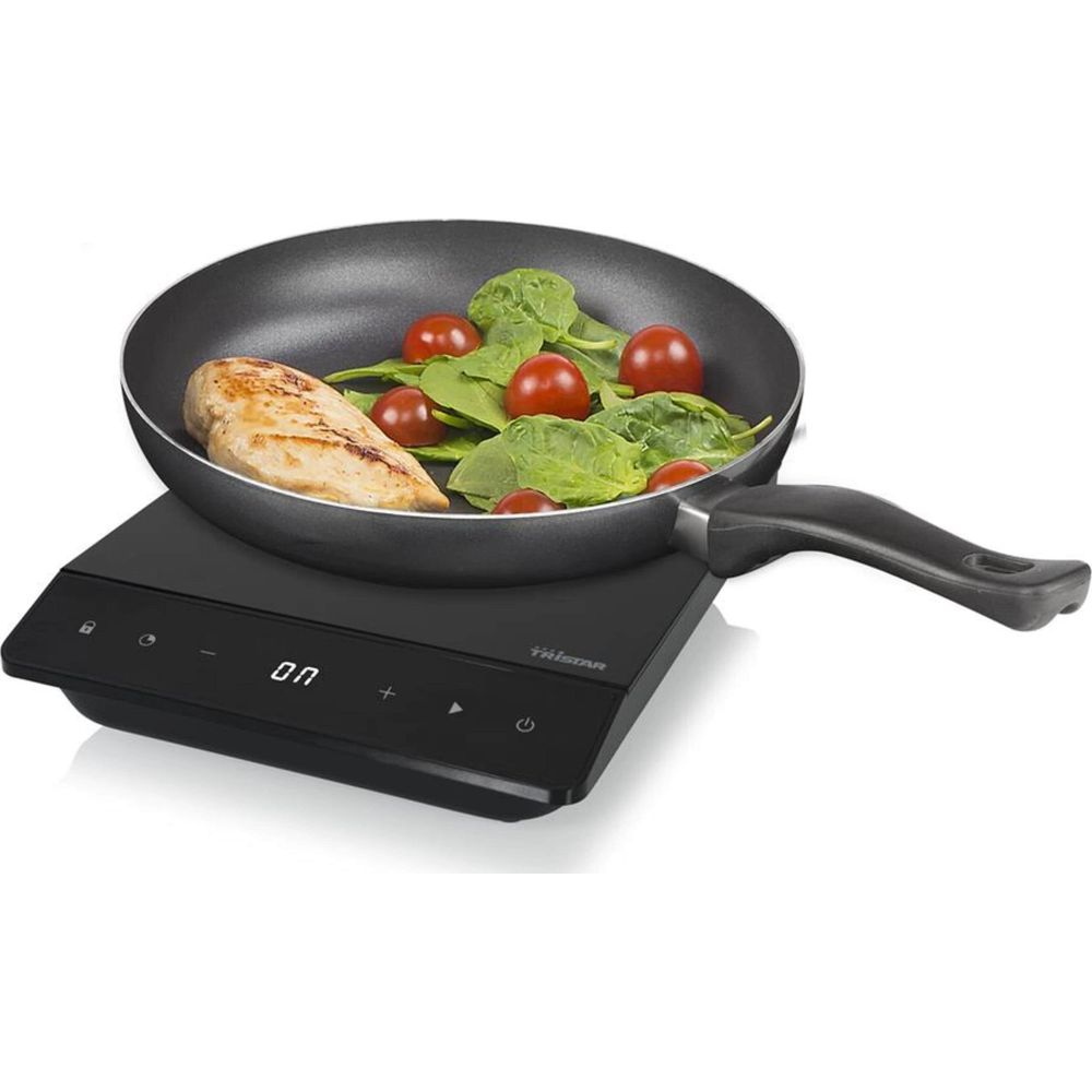 Un petto di pollo con spinaci e pomodori in padella su un piano cottura a induzione.