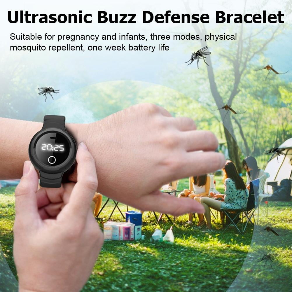 Armbanduhr mit Mückenschutz auf einer Hand, Camper im Hintergrund.