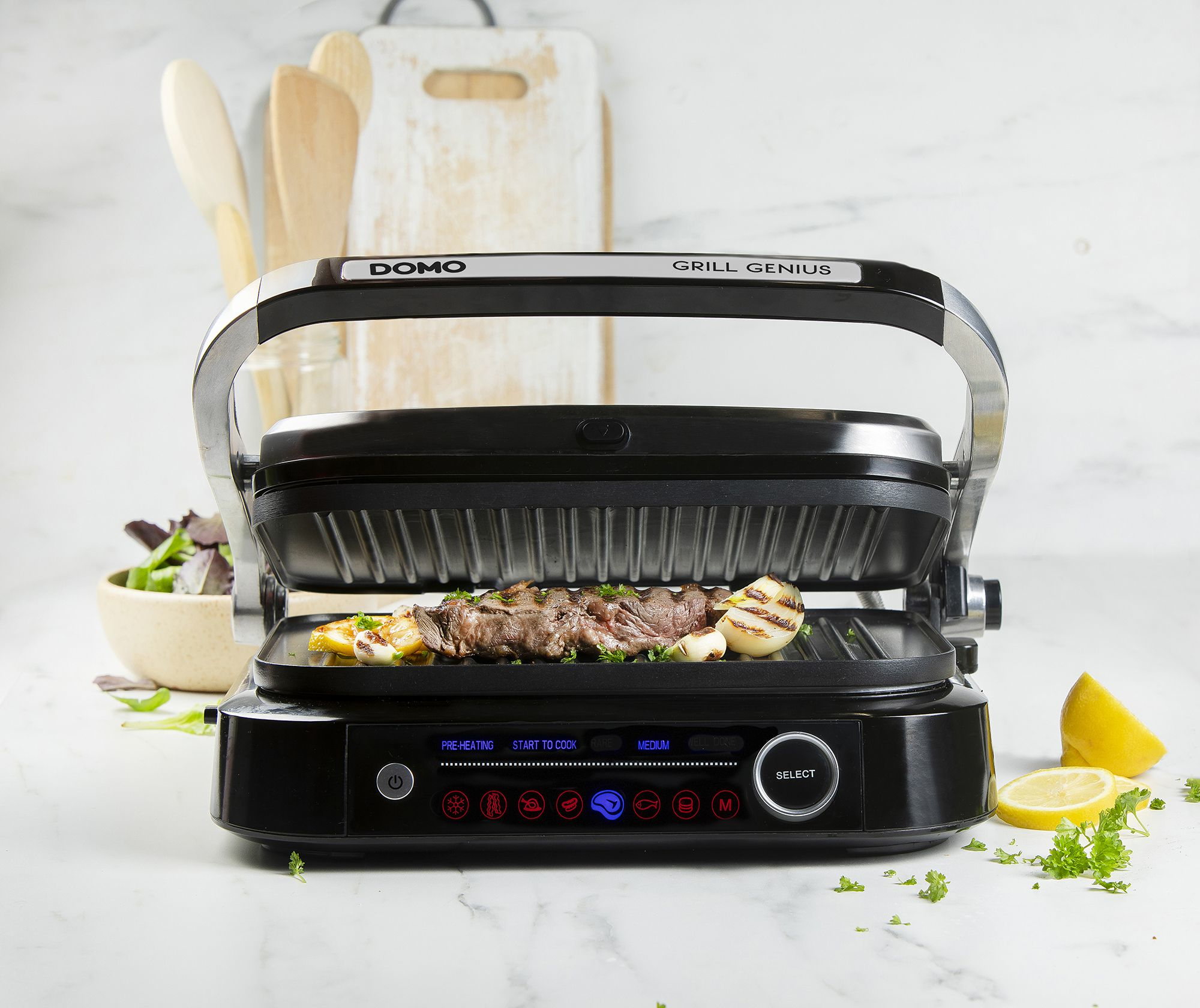 Ein geöffneter Elektrogrill mit Steak, Zwiebeln und Kartoffeln. Zitrone und Petersilie daneben.
