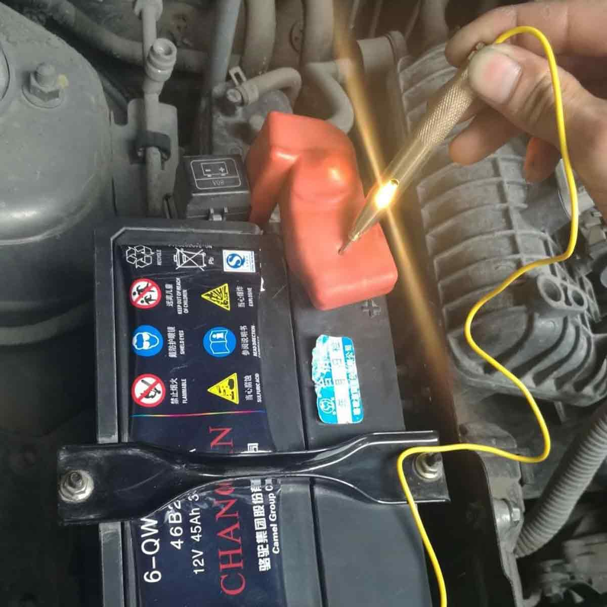 Ein Mann testet eine Autobatterie mit einem Stromprüfer. Der Prüfer leuchtet.