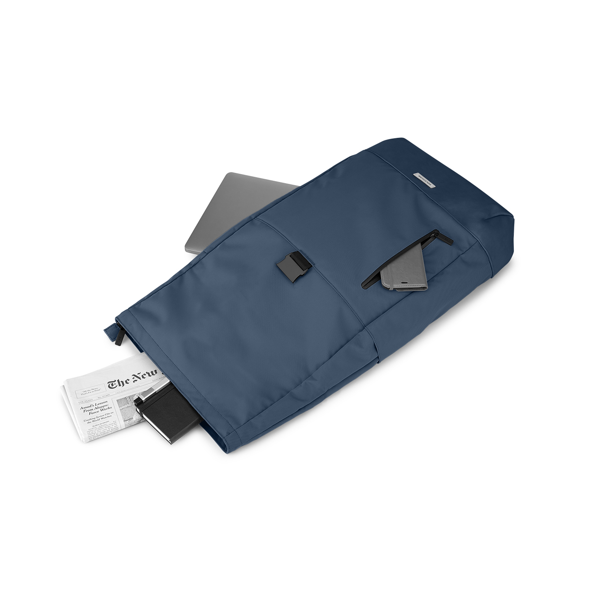 Uno zaino blu con laptop, telefono e giornale. Su sfondo bianco.