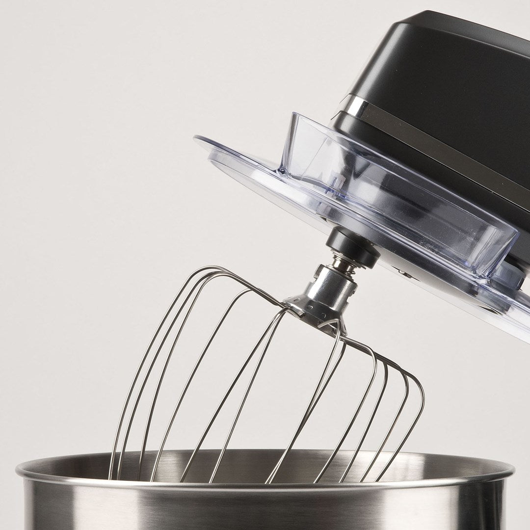 Primo piano di un robot da cucina nero con frusta in una ciotola di acciaio inox.
