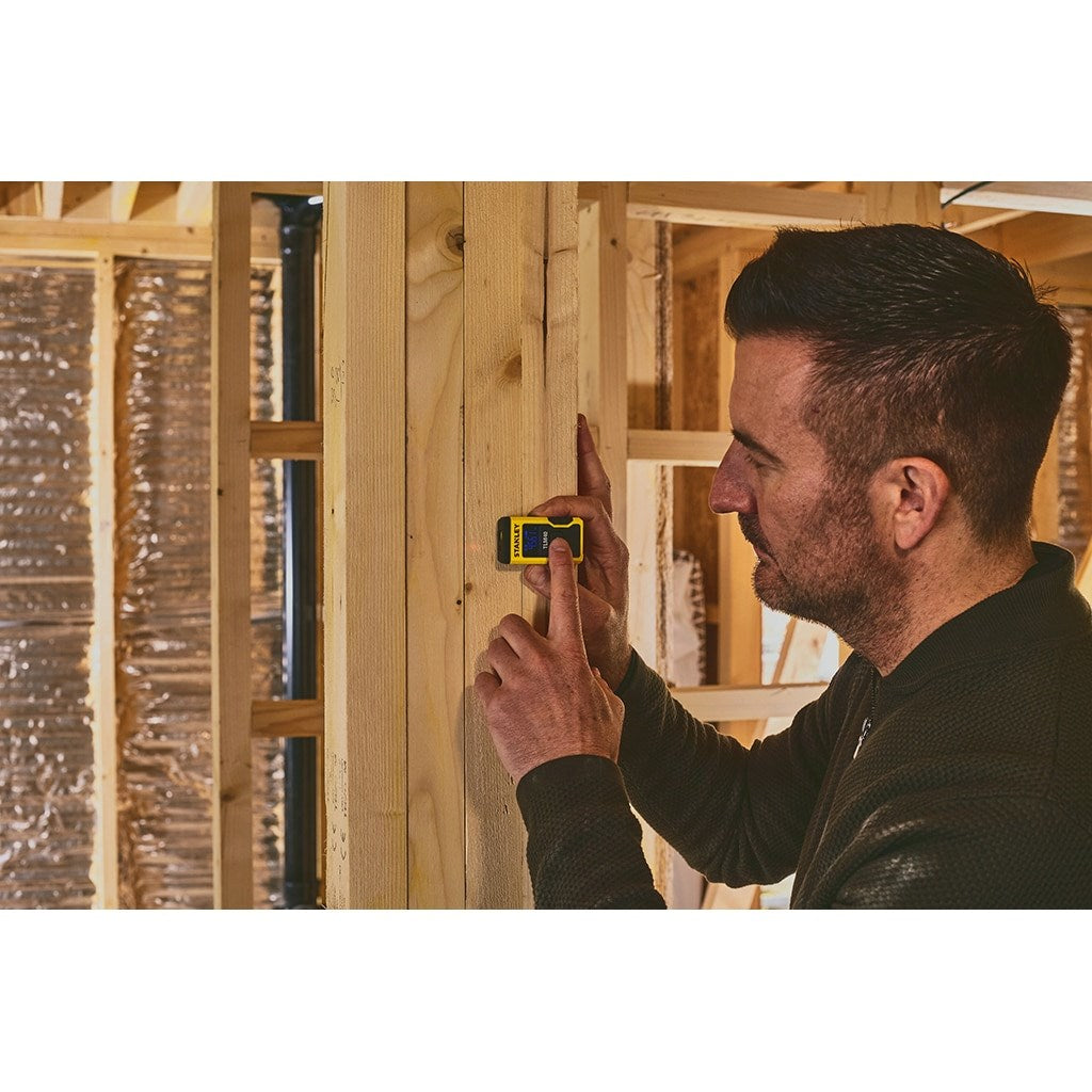 Mann mit Maßband an Holzwand in einem Rohbau.