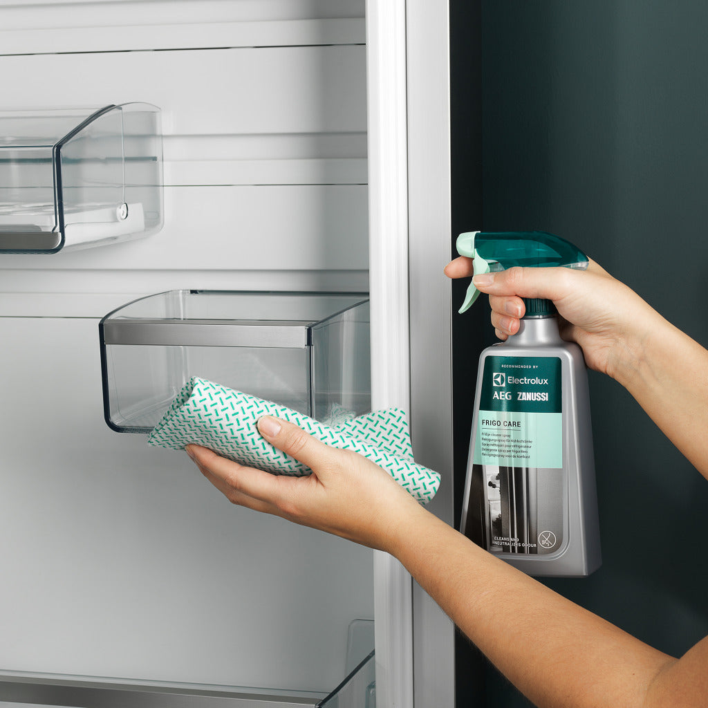 Persona pulisce interno frigorifero con panno e spray.