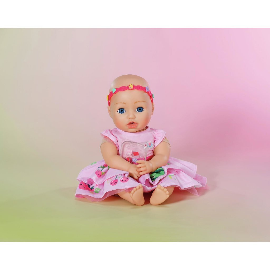 Una bambola neonata con occhi blu e vestito rosa con ciliegie seduta su sfondo sfumato.