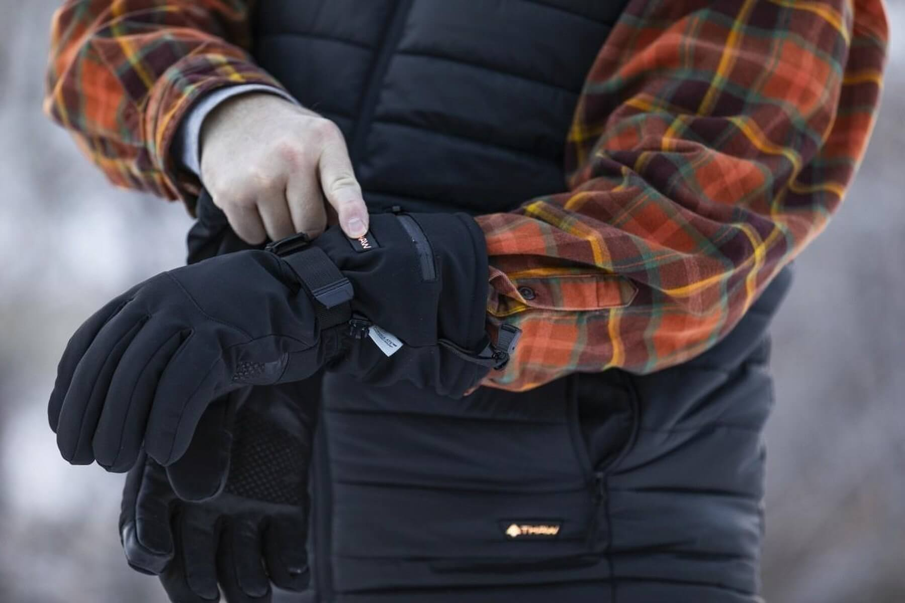 Uomo indossa guanti neri sopra camicia a quadri e gilet.