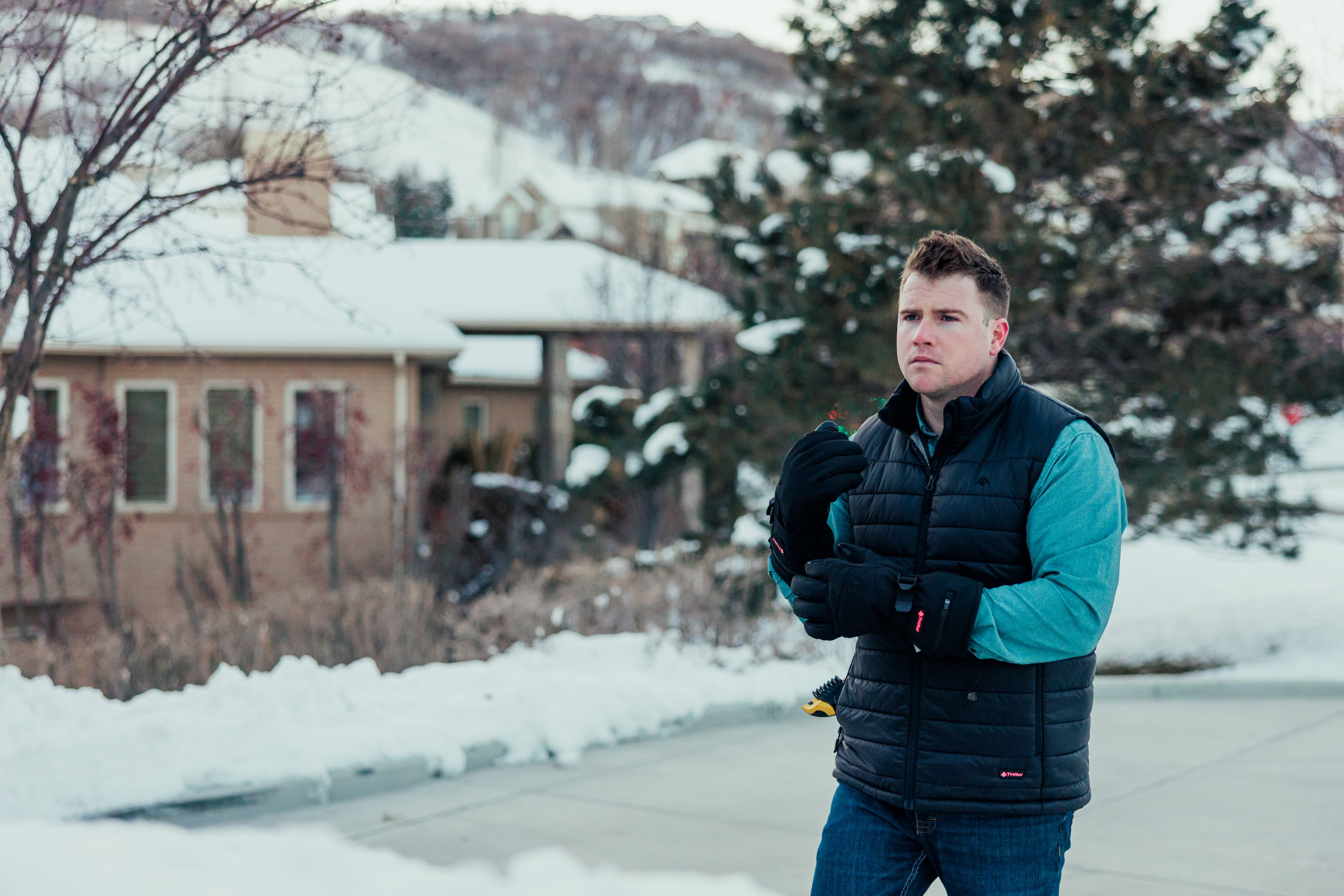 Uomo in gilet nero e camicia blu, inverno, neve, case sullo sfondo.