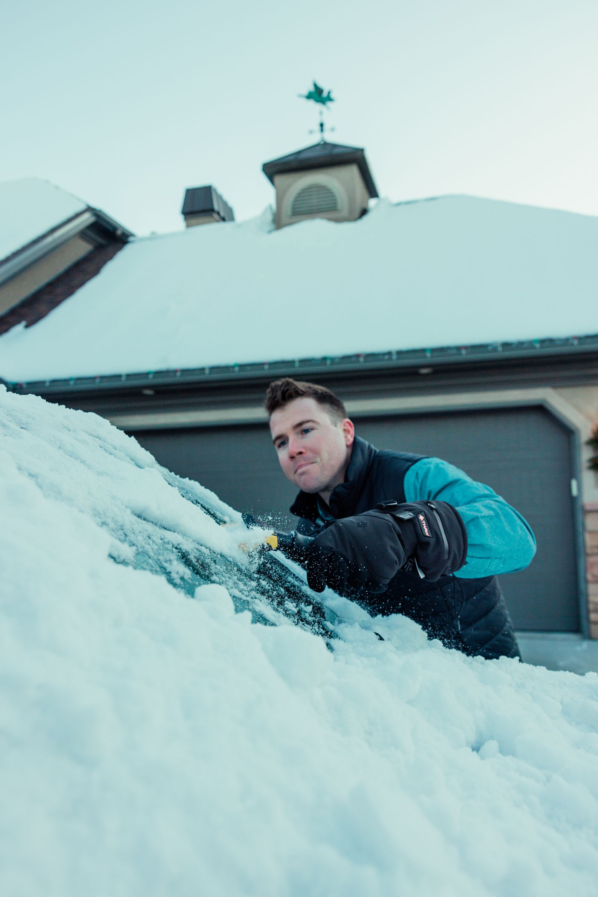 Uomo che raschia la neve dal parabrezza, indossa una giacca blu e nera.