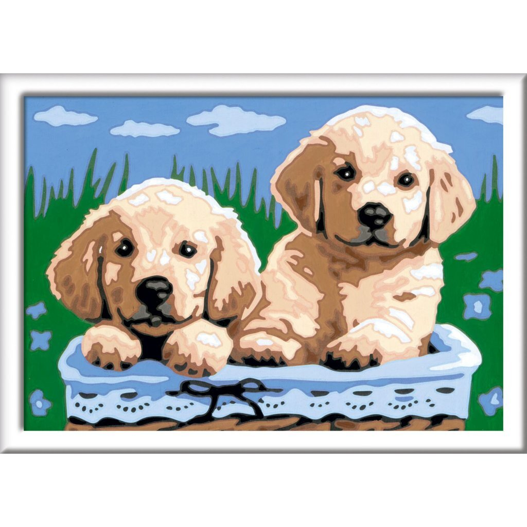 Dos cachorros dorados sentados en una cesta azul ante hierba verde y cielo azul.