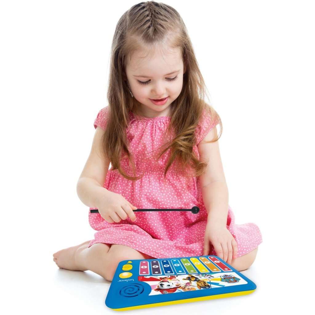 Una niña con vestido rosa toca un xilófono de juguete con personajes de Paw Patrol.