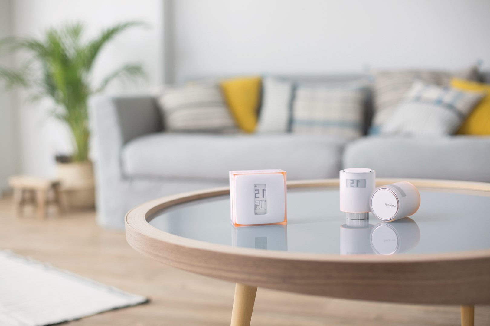 Two smart thermostats and a digital thermometer on a glass table in a living room.