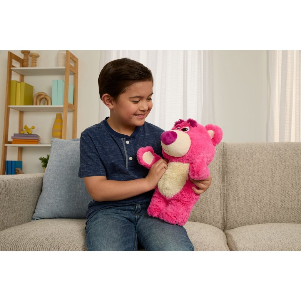 Un niño se sienta en un sofá sosteniendo un oso de peluche rosa.
