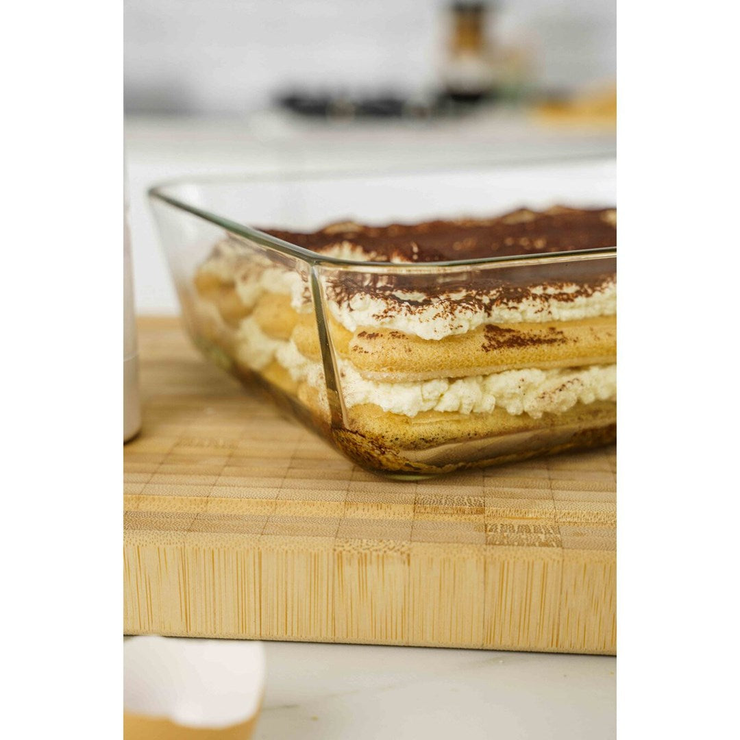 Un tiramisú en un recipiente de vidrio sobre una tabla de madera, espolvoreado con cacao.