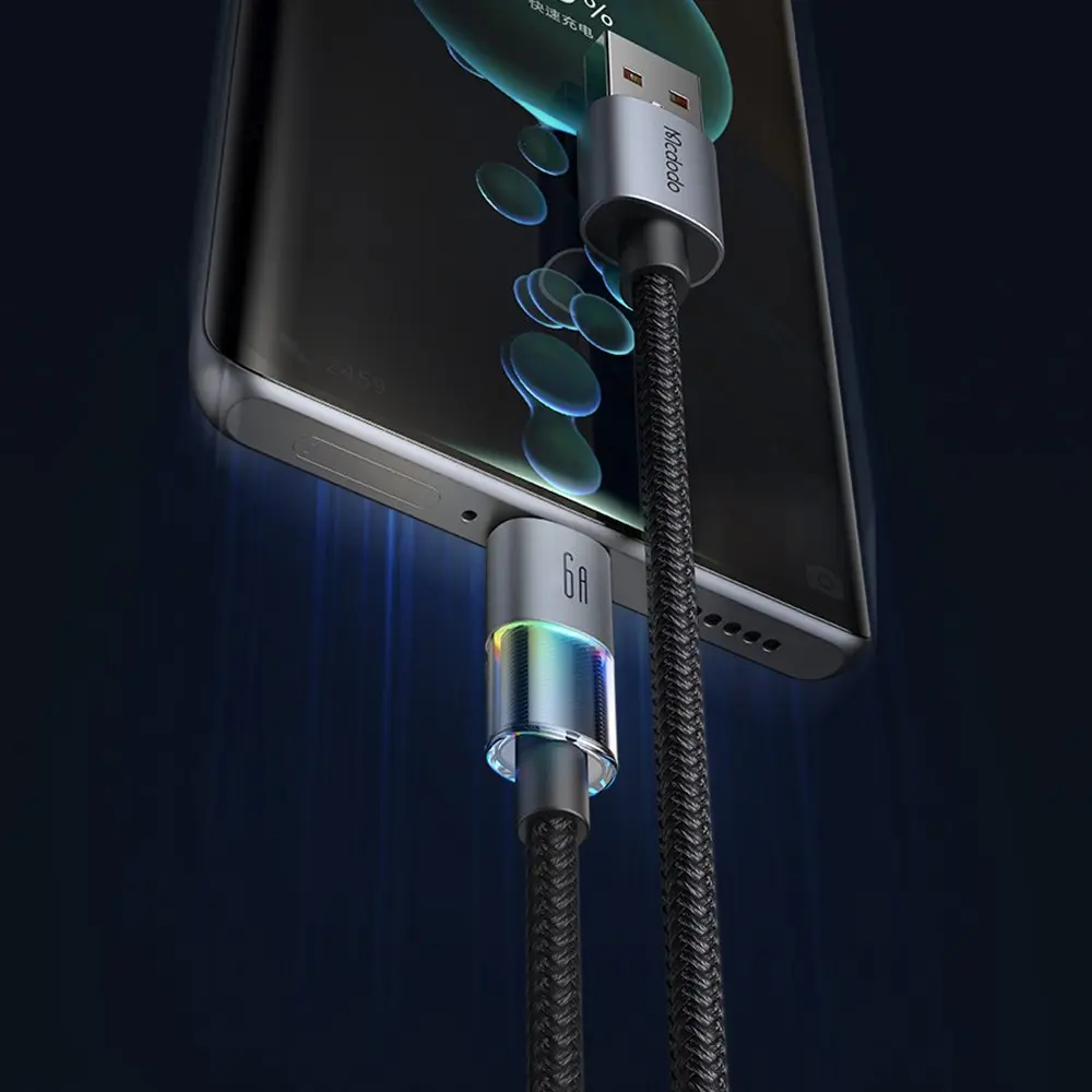 Gümüş renkli bir telefon, örgülü siyah kablo ile şarj oluyor. Konektör parlıyor.
