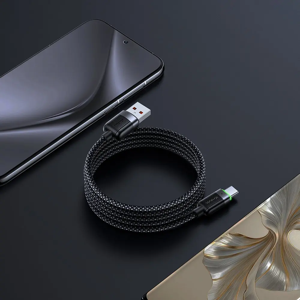 Siyah örgülü USB-C kablo, USB-A konektörüyle iki akıllı telefonun yanında karanlık yüzeyde duruyor.