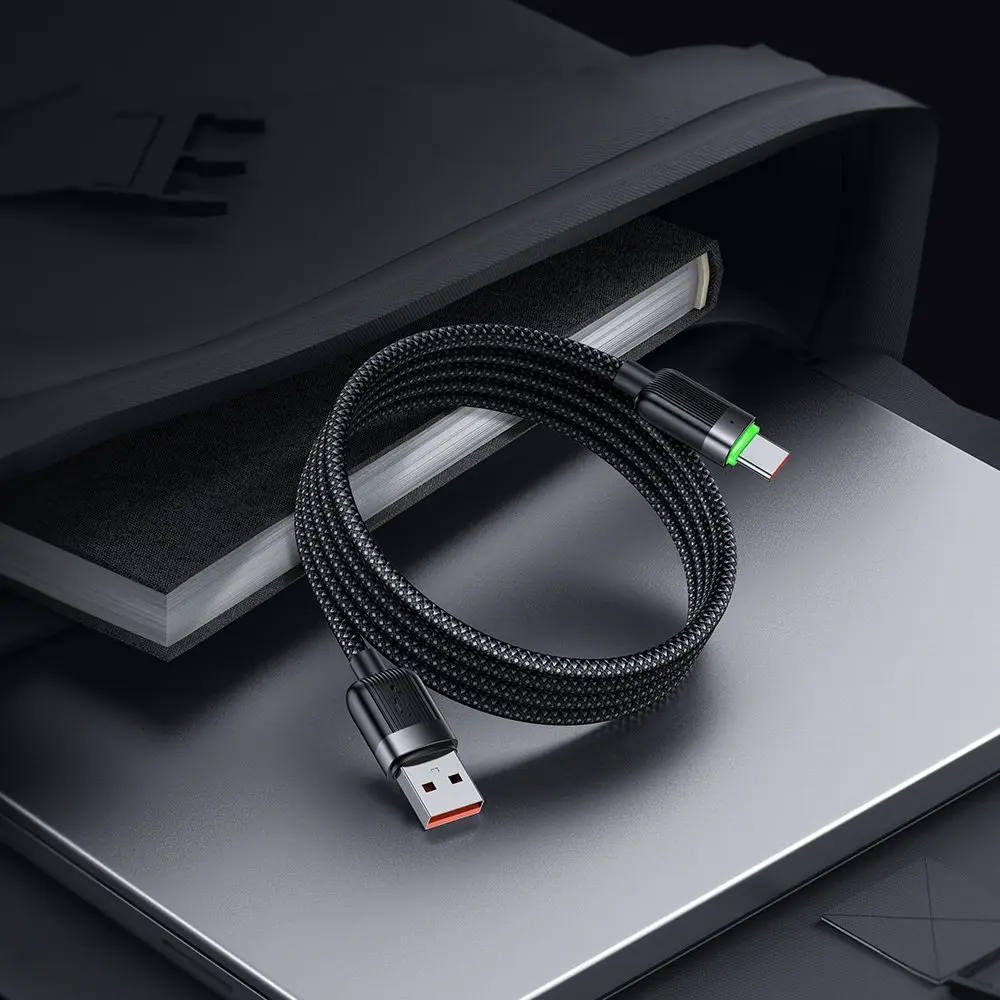 Siyah, örgülü USB-C kablo, kırmızı/yeşil vurgulu, kitap ve dizüstü bilgisayar üzerinde.
