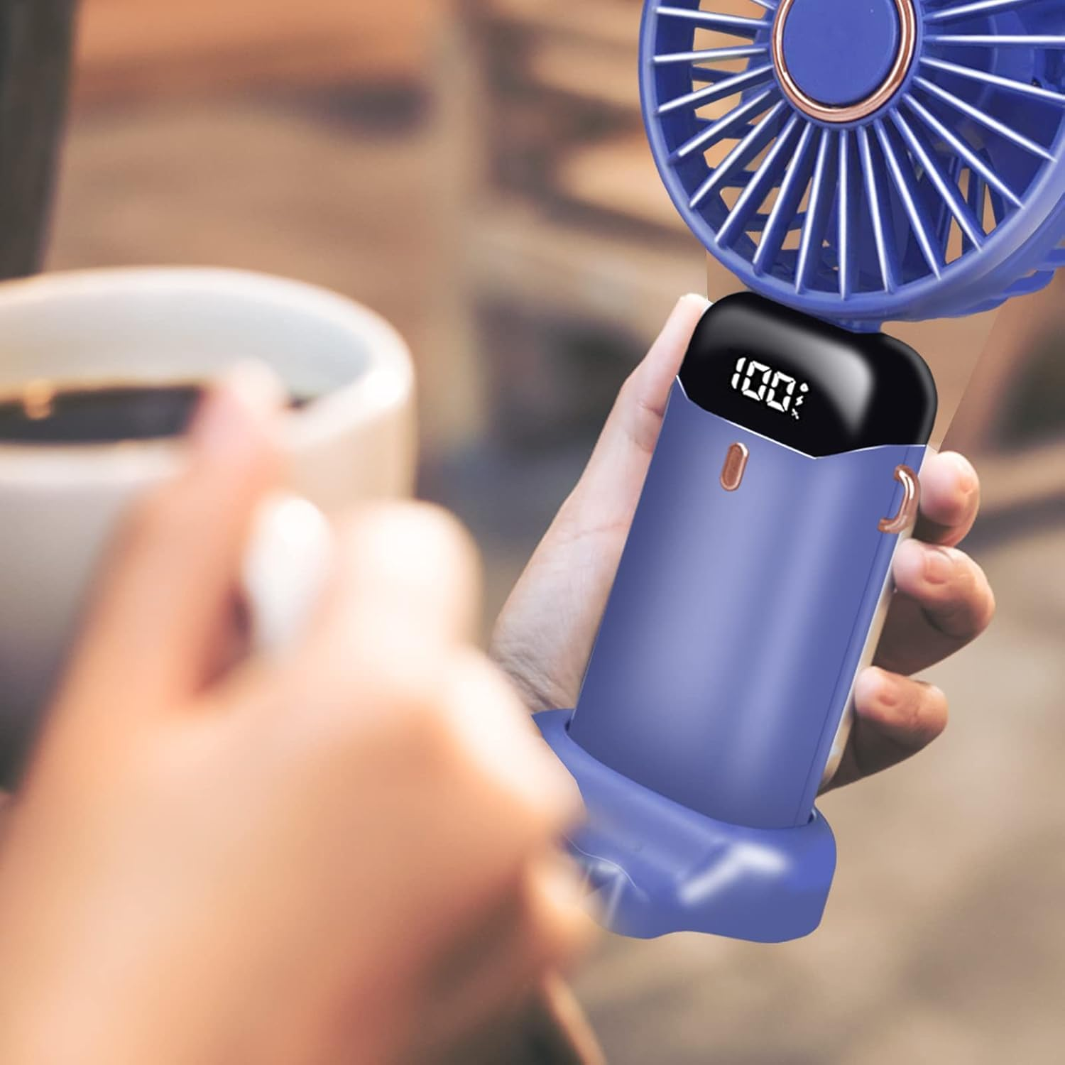 Eine Hand hält einen blauen Mini-Ventilator mit digitaler Anzeige (100%).