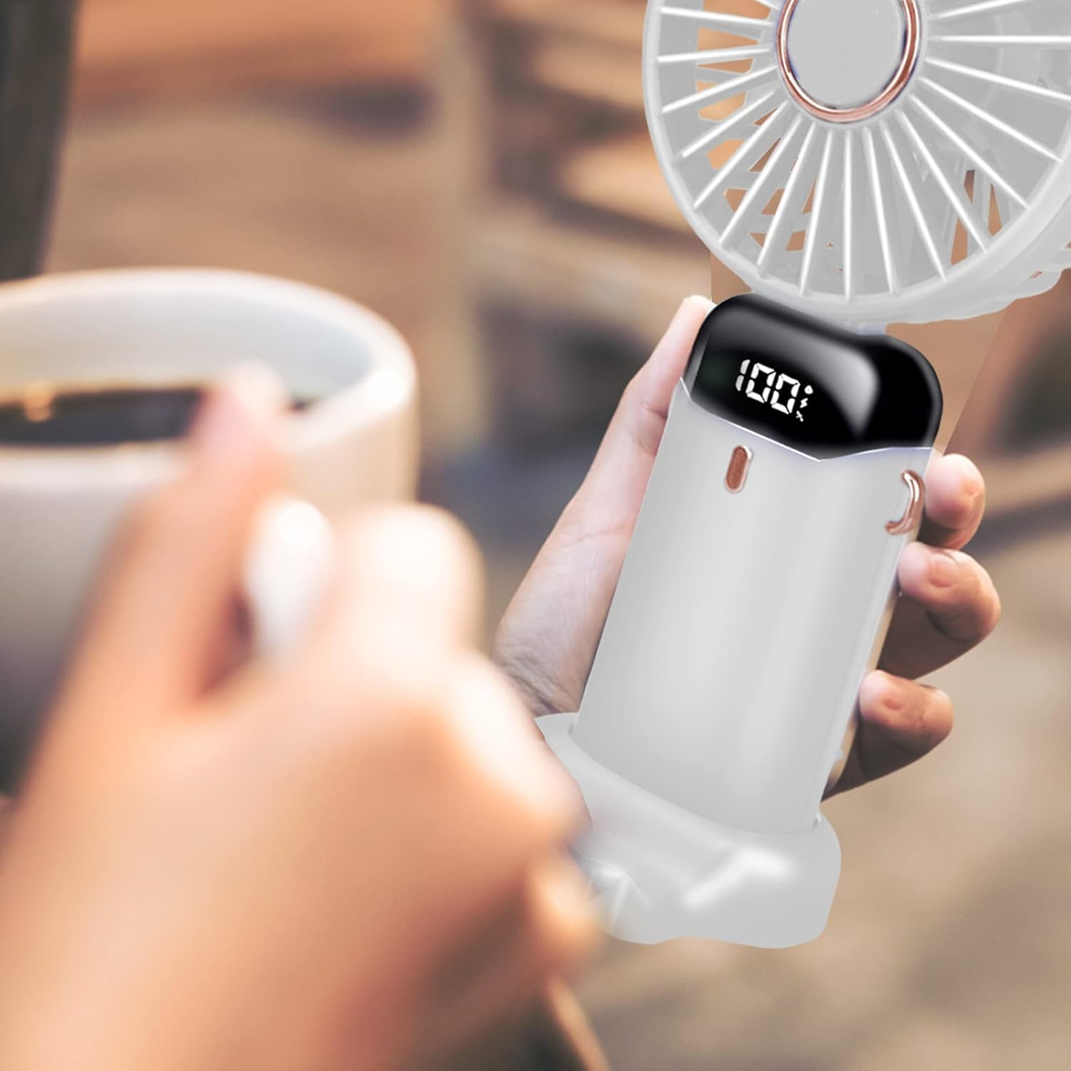 Eine Hand hält einen weißen Handventilator mit 100 % Batteriestatusanzeige.
