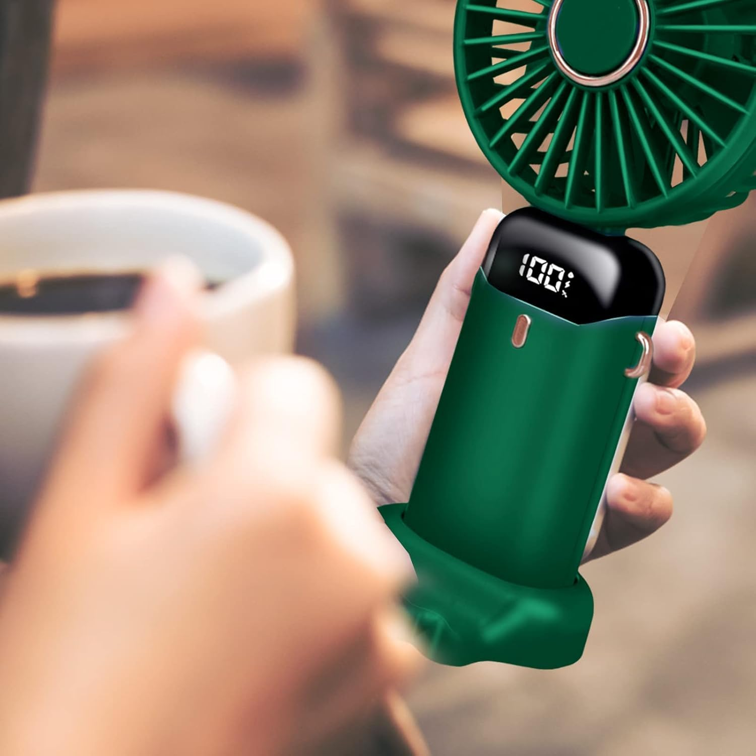 Grüner Handventilator mit digitaler Anzeige (100%) wird von Händen gehalten.