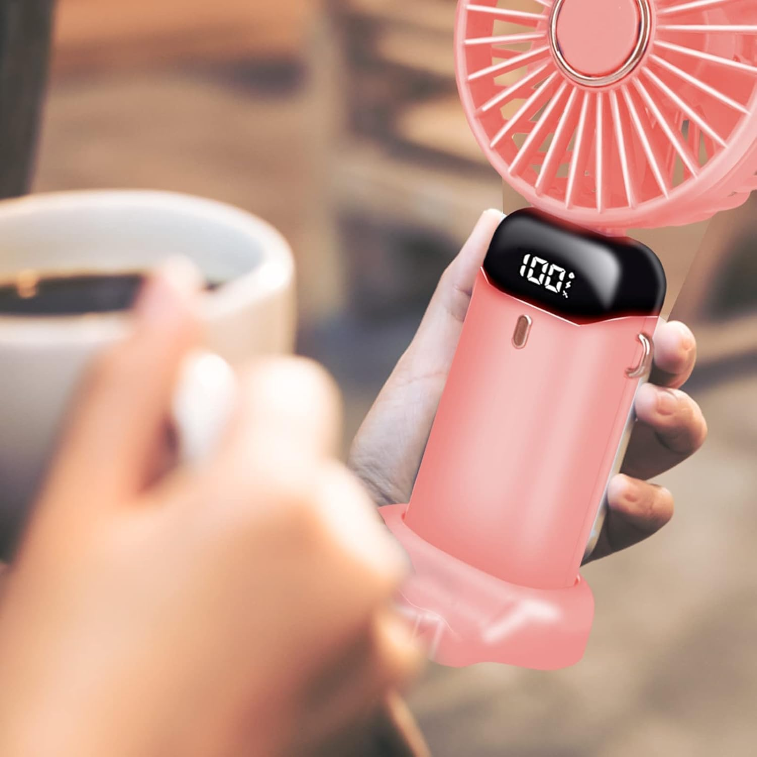 Eine Hand hält einen rosafarbenen Mini-Ventilator mit digitaler Anzeige.