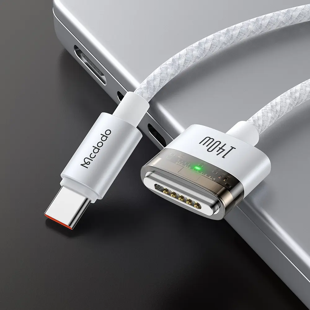 Mıknatıslı konektörlü beyaz bir USB-C kablosu gümüş bir dizüstü bilgisayarın üzerinde duruyor.