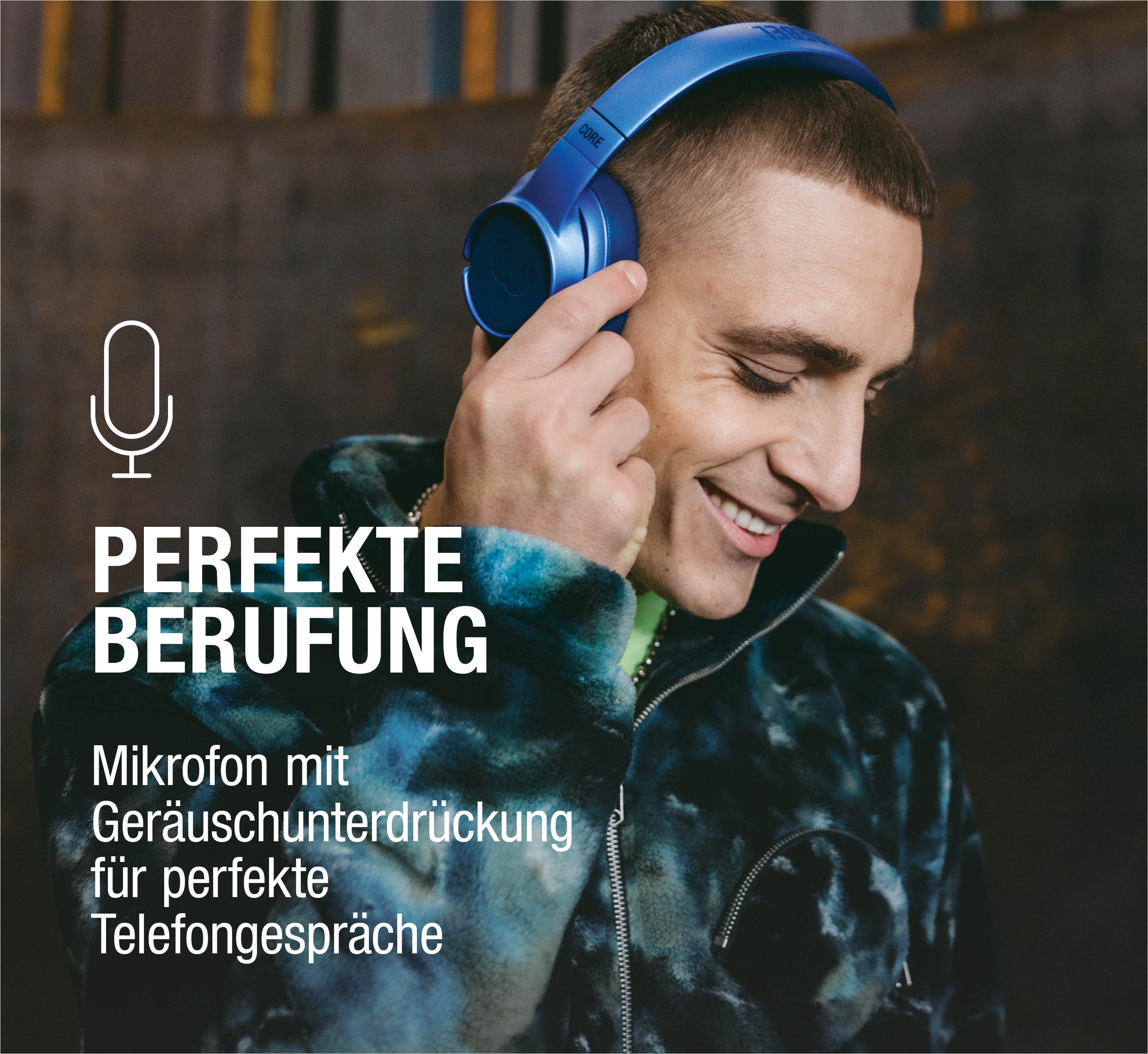 Mann mit blauen Kopfhörern lächelt, trägt ein buntes Hemd.