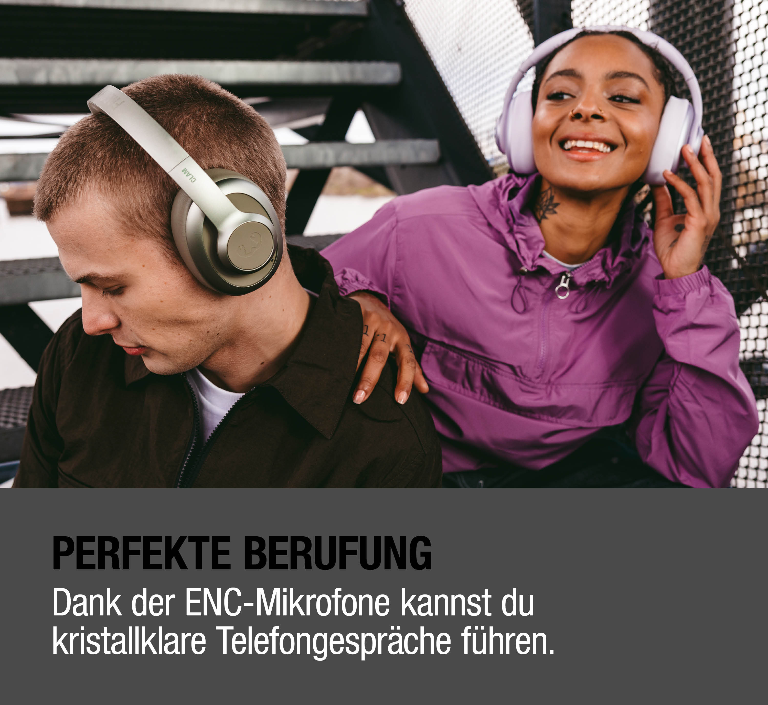 Zwei Personen mit Kopfhörern sitzen draußen. Ein Mann schaut nach unten, eine Frau lächelt.