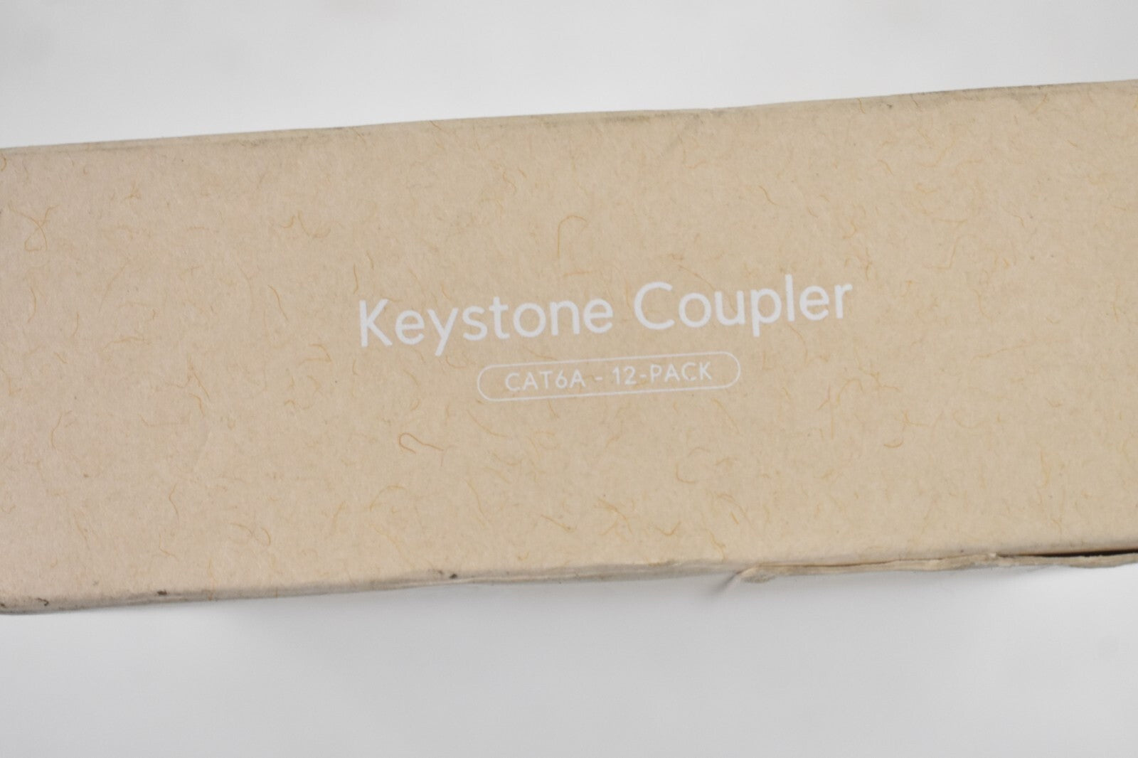 Scatola con testo "Keystone Coupler CAT6A - 12 PACK" su carta marrone chiaro.