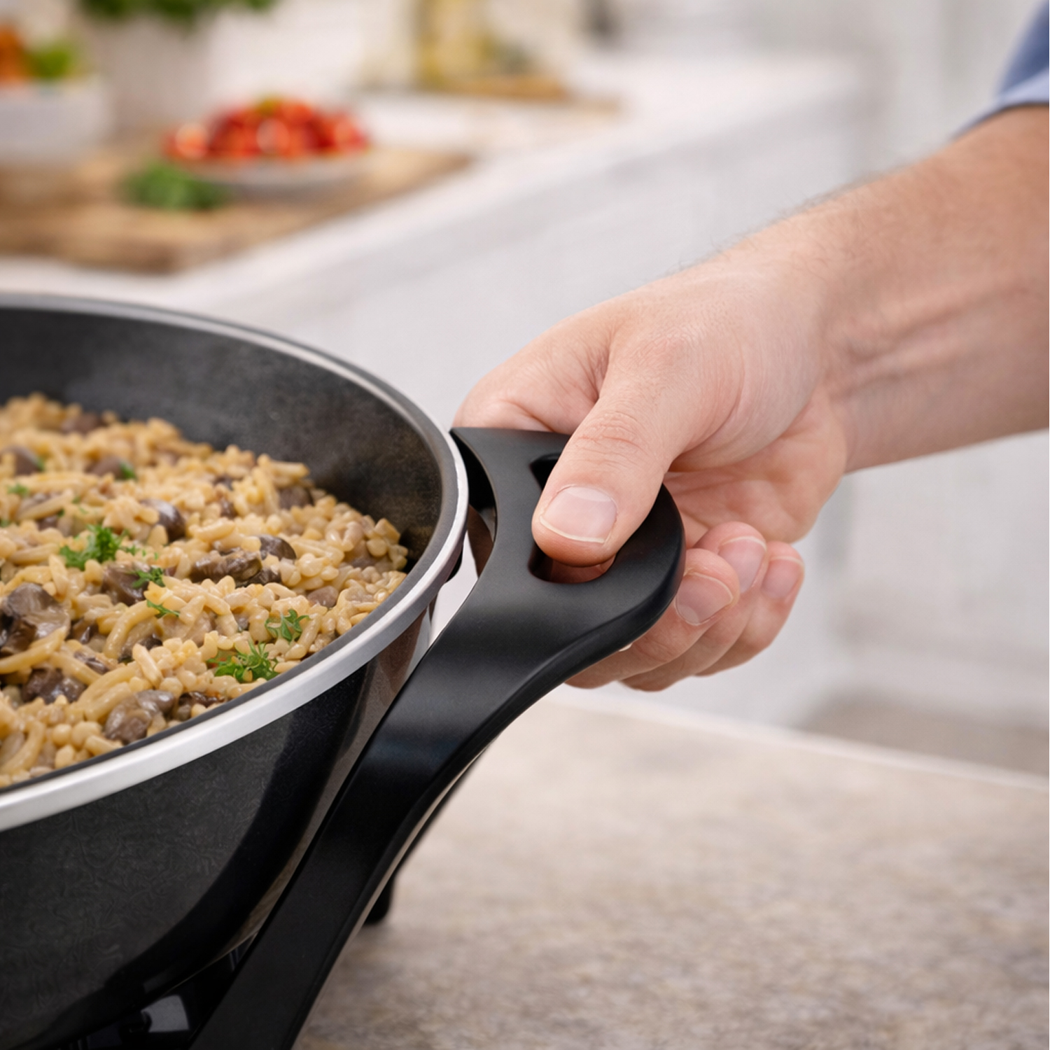 Una mano tiene il manico di una padella piena di riso e funghi.