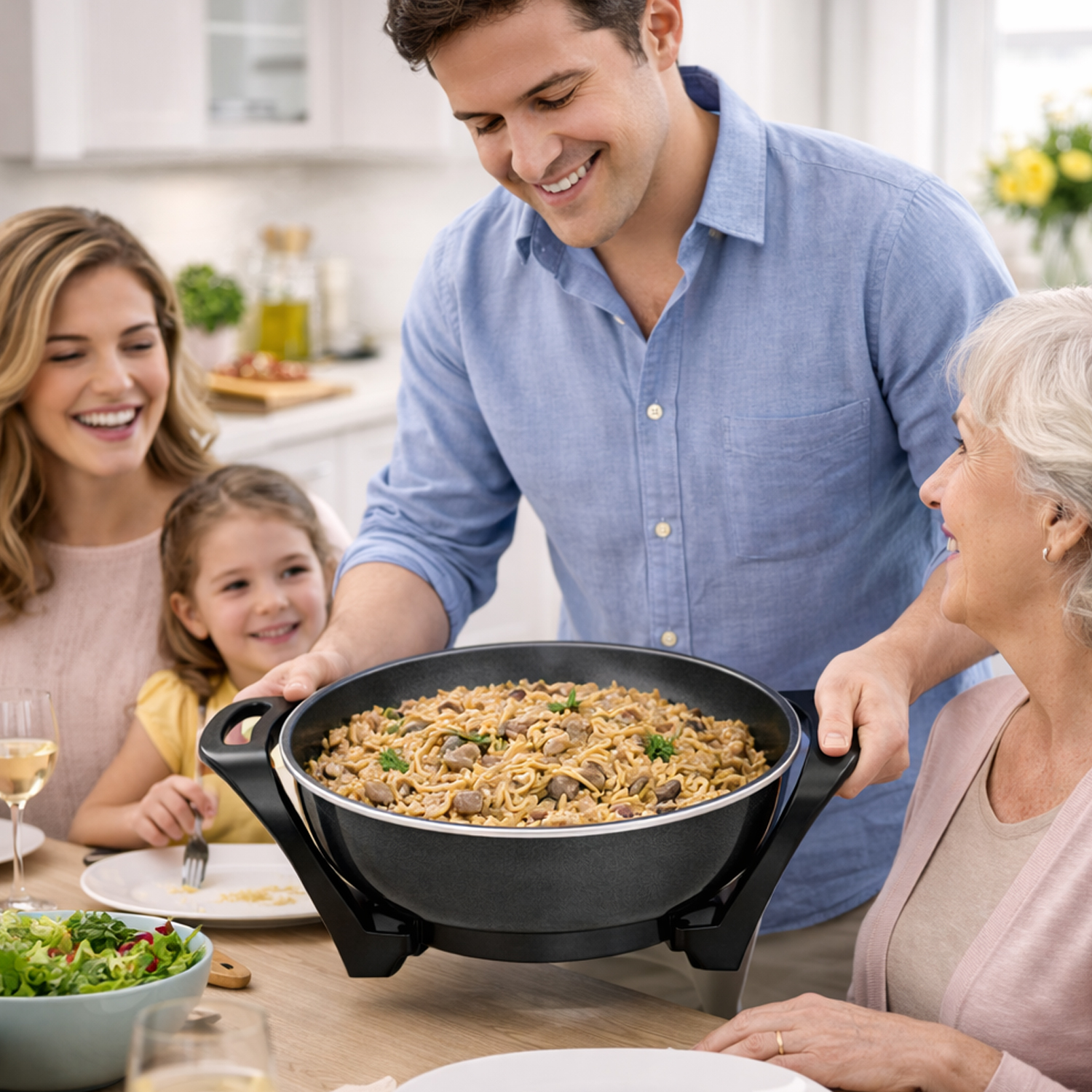 Un uomo serve una padella di noodles a una famiglia riunita attorno a un tavolo.