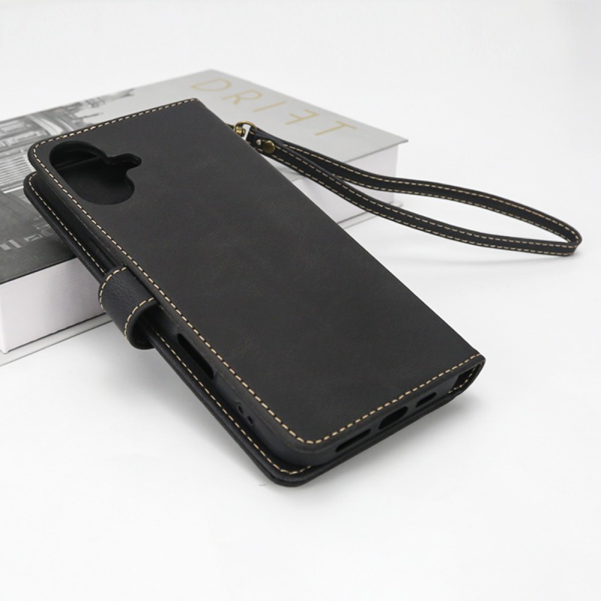 Custodia flip in pelle nera con cinturino da polso, su un libro.